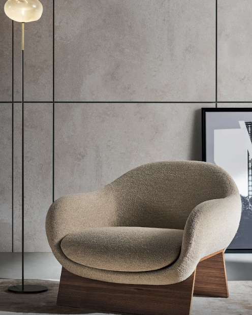 Elegant beige curved armchair with wooden base against concrete wall